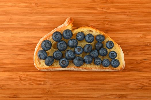 Wooden bamboo cutting board with sandwich of mellow blueberries on slice of wheat bread