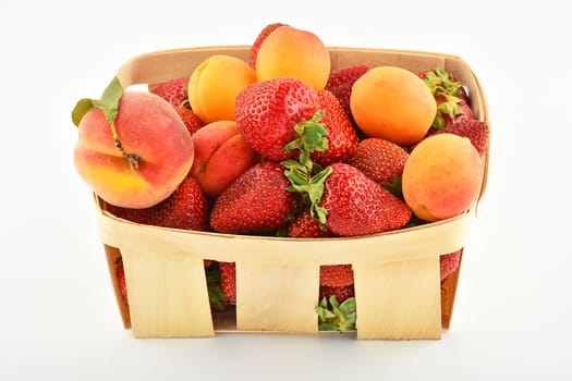 Mellow fresh summer strawberries, apricots and peach in wooden basket isolated on white background