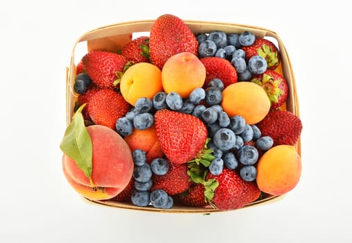 Mellow fresh summer strawberries, blueberries, apricots and peach in wooden basket isolated on white background, top view