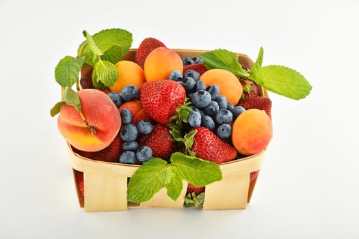Mellow fresh summer strawberries, blueberries, apricots, peach and mint leaves in wooden basket isolated on white background
