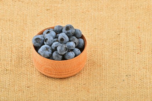 Handful of fresh blueberries in handmade wooden bowl on burlap jute canvas