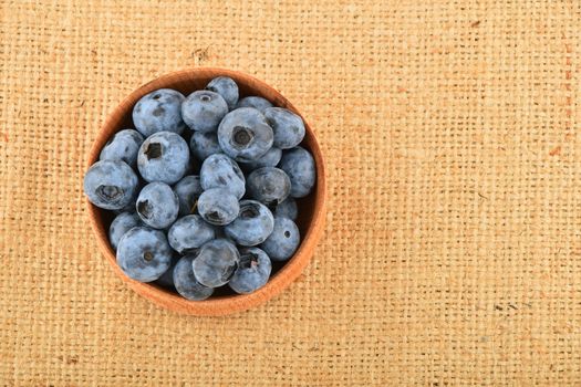 Handful of fresh blueberries in handmade wooden bowl on burlap jute canvas, top view