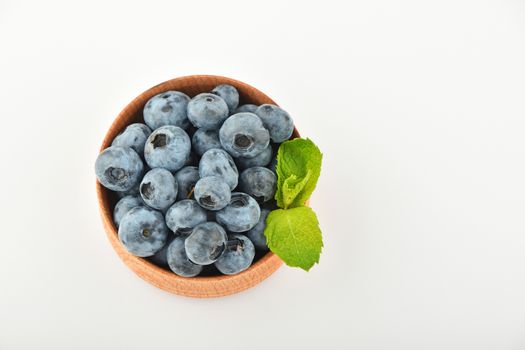 Handful of fresh blueberries with mint leaves in handmade wooden bowl isolated on white, top view