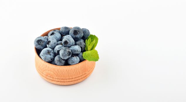 Handful of fresh blueberries with mint leaves in handmade wooden bowl isolated on white