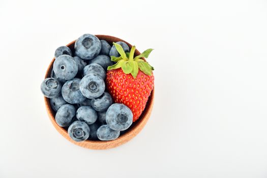 Handful of fresh blueberries and one strawberry in handmade wooden bowl isolated on white, top view