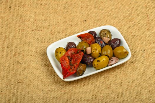 White plate of Mediterranean snack of red and green olives and pickled red pepper on burlap jute canvas