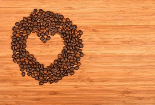 Heart shaped coffee beans round frame of Roasted Arabica coffee espresso beans over wooden bamboo board background