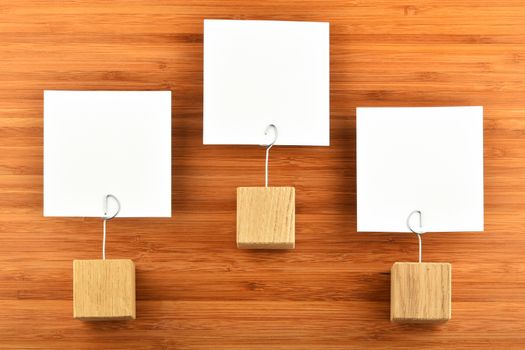 Hierarchy - Three white paper notes with wooden holders isolated bamboo wooden background for presentation