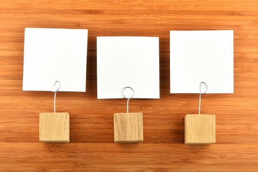 Three white paper notes with wooden holders on bamboo wooden background for presentation