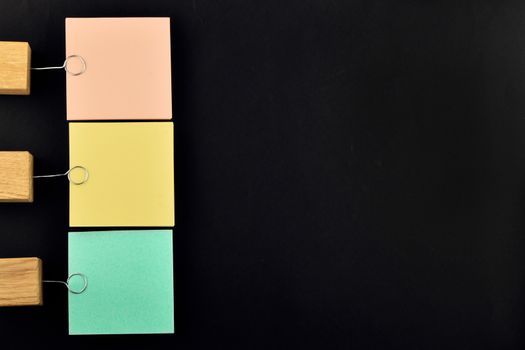 List, three paper notes, green, yellow, pink, with wooden holder isolated on black paper background for presentation