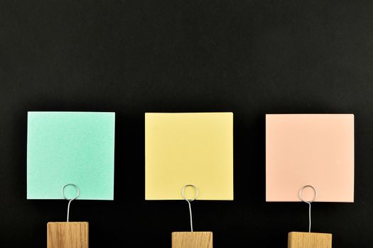 Three paper notes, green, yellow, pink, with wooden holder isolated on black paper background for presentation
