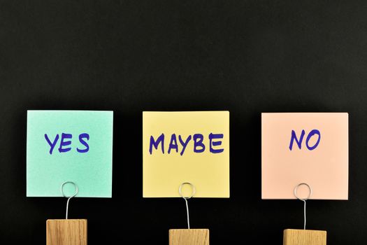 Yes, no, maybe, three paper notes, green, yellow, pink, with wooden holder isolated on black paper background for presentation