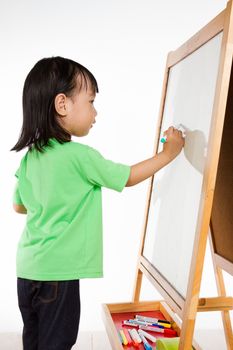 Happy cute Asian Chinese toddler girl drawing or writting with marker pen on a blank whiteboard at home, preschool, daycare or kindergarten in plain white isolated background.