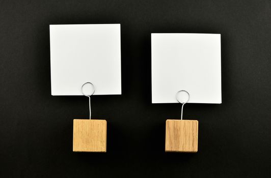 Two white paper notes with wooden holders isolated at black paper background for presentation
