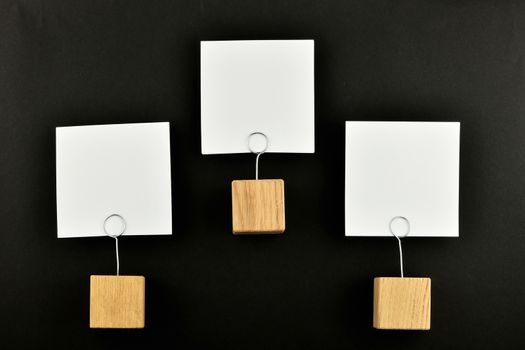 Hierarchy - Three white paper notes with wooden holders isolated at black paper background for presentation