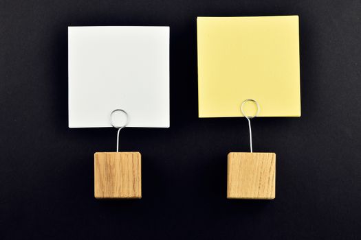 Two paper notes (white & yellow) with wooden holders isolated at black paper background for presentation