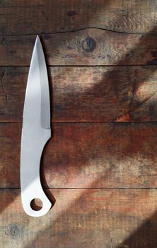 One throwing knife on nice wooden background under beam of sunlight