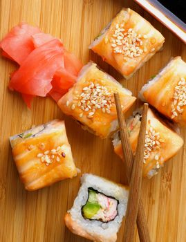 Delicious Salmon Maki Roll with Crab, Cucumber, Sesame Seeds and Soy Sauce, Ginger and Chop Sticks closeup on Straw Mat. Top View