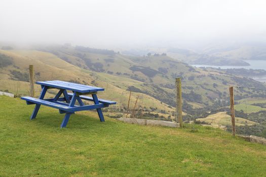 Lonely Blue Picnic table in lush green park on scenic viewpoint of Akaroa, New Zealand.