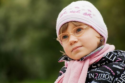 Pretty  child girl in glasses sits on a Park bench