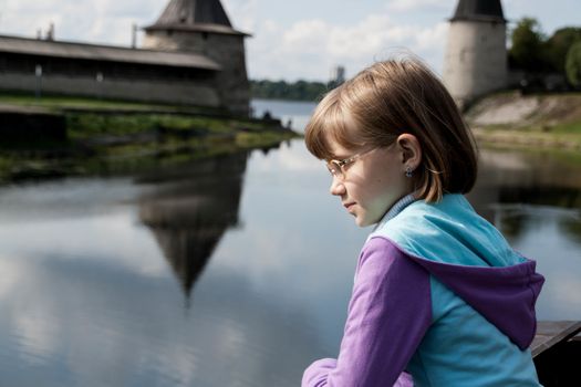  blonde girl looks thoughtfully at the river on the background of the Pskov Kremlin
