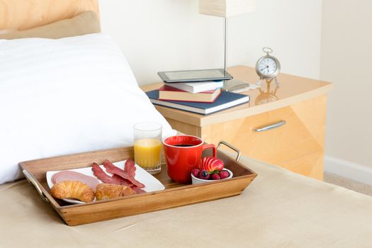 Relaxing breakfast in bed with coffee, fresh berries, croissants and bacon and a time to read with a pile of assorted books on the bedside cabinet