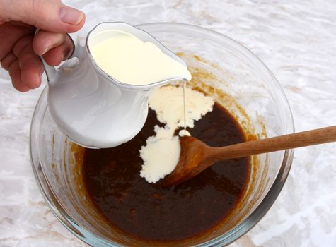 Pouring heavy cream from a jug into pumpkin pie filling in a bowl