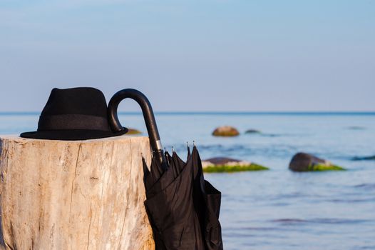 Black umbrella and hat on the wooden stump at the seashore