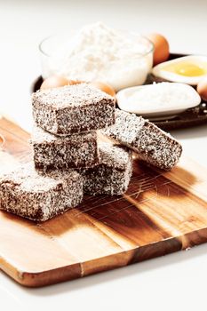 Group of Lamingtons on a timber metal baking tray with food ingredients in the background