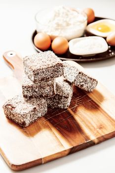 Group of Lamingtons on a timber metal baking tray with food ingredients in the background