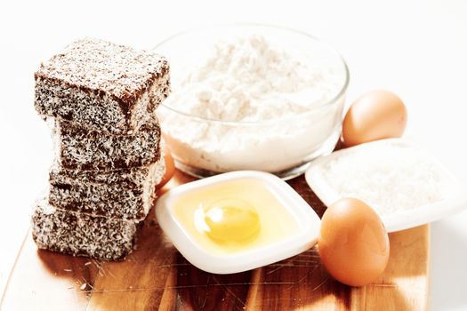 Group of Lamingtons on a timber metal baking tray with food ingredients in the background