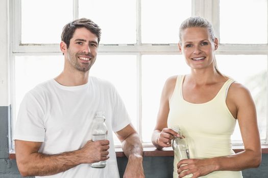 Couple holding bottle of water posing in crossfit gym