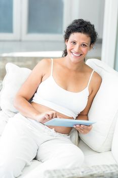 Portrait of happy pregnant woman using tablet while sitting on sofa
