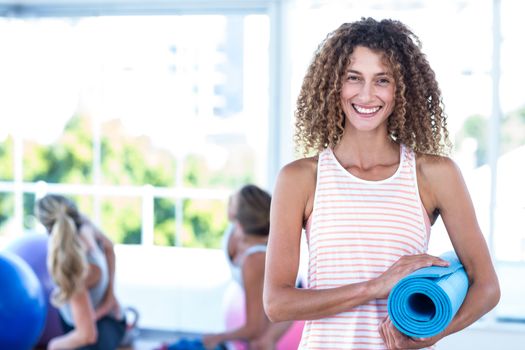 Portrait of woman smiling while holding exercise mat in fitness studio