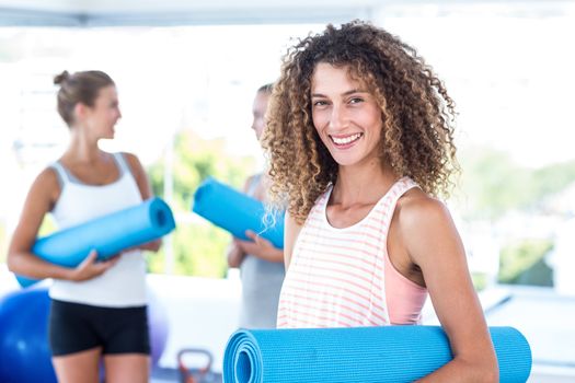 Portrait of smiling woman holding yoga mat in fitness studio