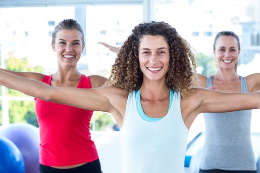 Portrait of women smiling with arms outstretched in fitness studio