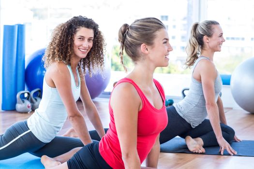 Women smiling while doing pigeon posture in fitness studio