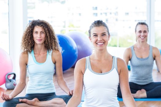 Portrait of women smiling while doing lotus pose in fitness studio