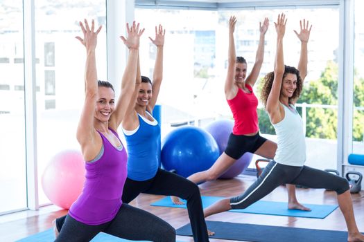 Portrait of cheerful women doing low warrior pose in fitness studio on exercise mat