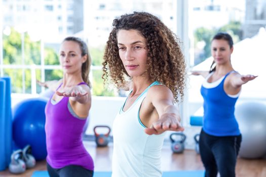Focused women doing warrior II pose in fitness studio