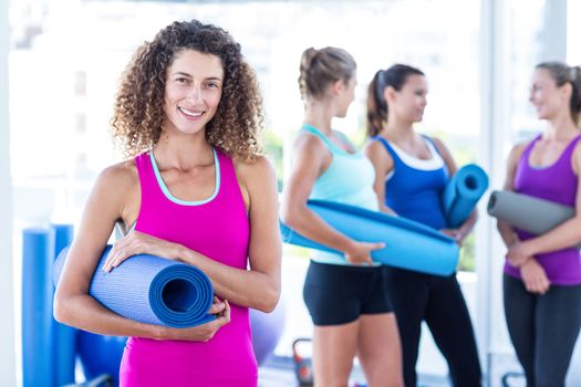 Portrait of a woman smiling while holding exercise mat in fitness studio