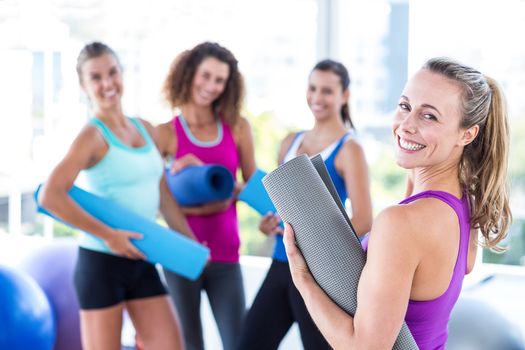 Portrait of a cheerful woman holding exercise mat in fitness studio