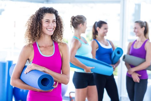 Woman smiling while holding exercise mat in fitness studio