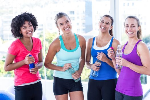 Portrait of fit women holding water bottle in fitness studio