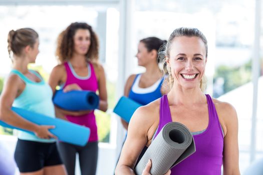 Portrait of cheerful woman holding exercise mat and smiling in fitness studio