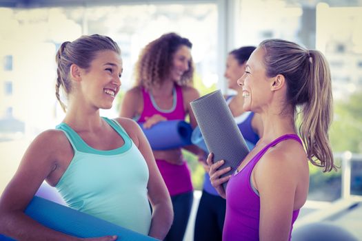Attractive women looking at each other and smiling while holding exercise mat in fitness studio