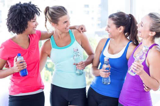 Cheerful women holding water bottle and smiling in fitness studio