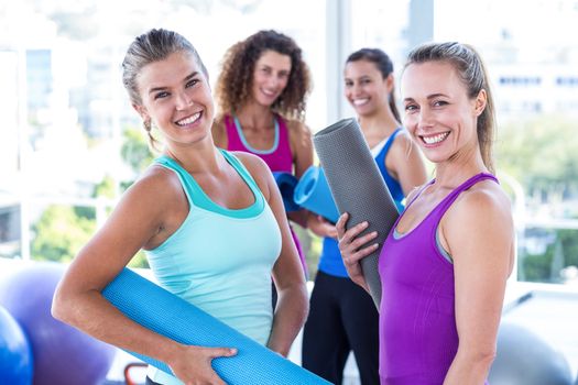 Portrait of attractive women holding exercise mat in fitness studio