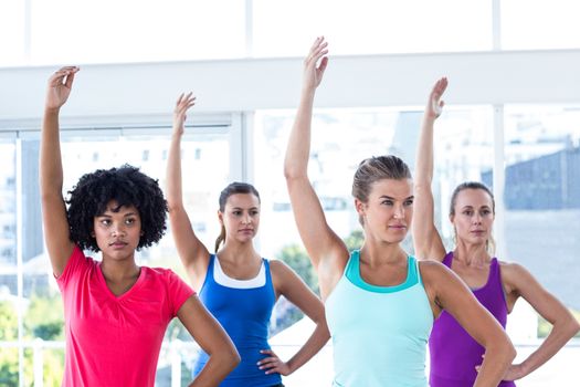 Focused woman in fitness studio with left arm raised while standing