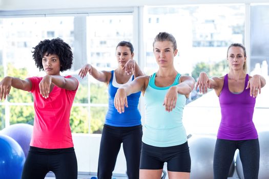 Serious women with arms stretched forward in fitness studio